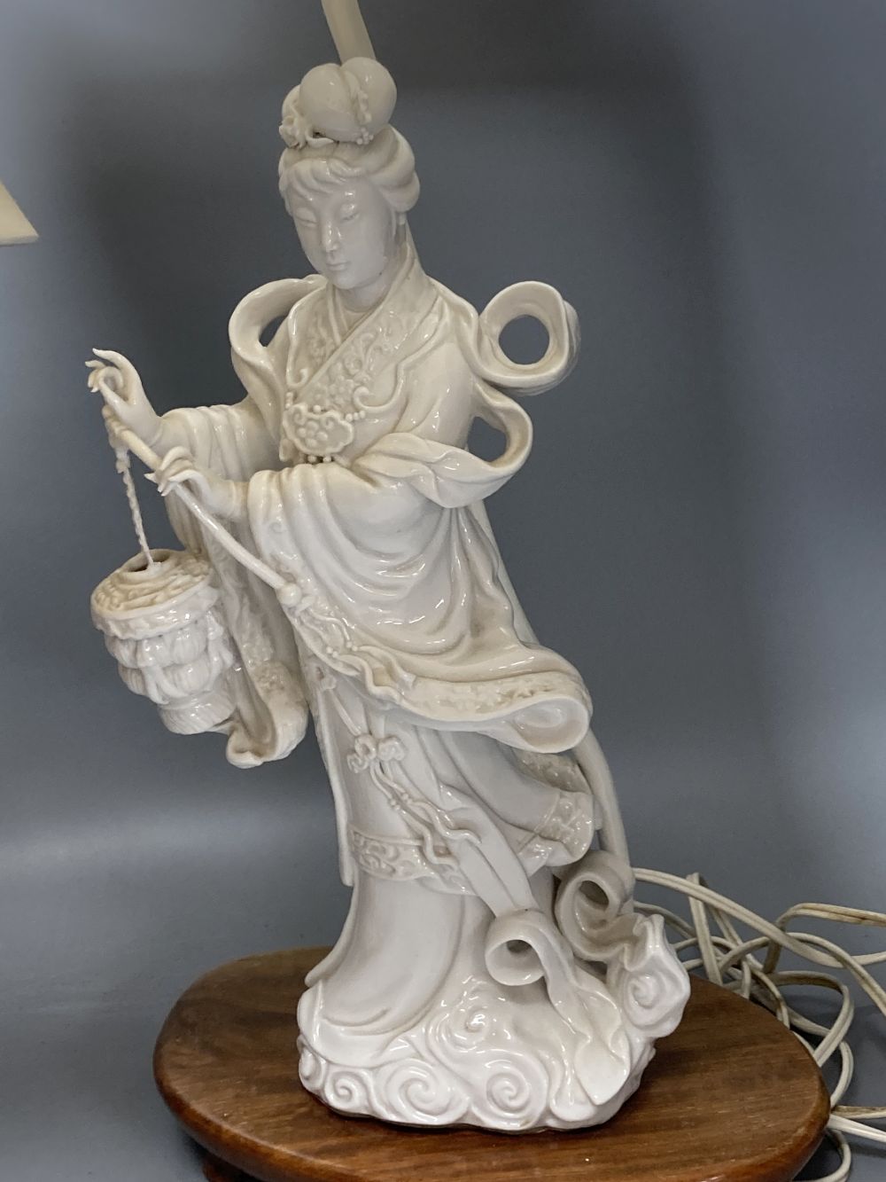 A Chinese blanc de chine porcelain table lamp, modelled as Guanyin, 65cm high including shade and a toleware vase shaped table lamp (2)